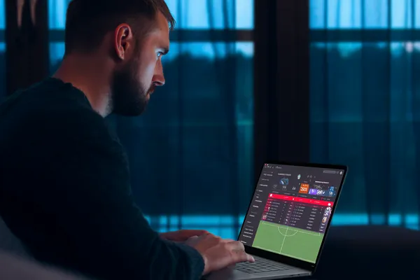 SINAGPH মোবাইল অ্যাপ — ক্যাসিনো ও স্পোর্টসের সম্পূর্ণ হাব একজন পুরুষ তার ল্যাপটপে মনোযোগ দিয়ে কাজ করছেন, ব্যাকগ্রাউন্ডে লাইভ স্ট্যাটস — যা SINAGPH মোবাইল অ্যাপের স্পোর্টস ও গেমিং ফিচারগুলোকে তুলে ধরে।