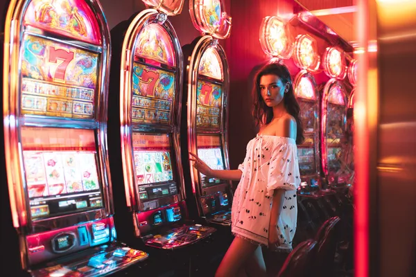 SINAGPH Slots — Thousands of exciting themes and jackpots A stylish woman beside vibrant slot machines displaying glowing sevens, showcasing the variety of top slots at SINAGPH.